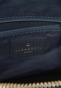 Marinekleurige binnenkant van een tas met een goud-embossed label met "LAZAROTTI" en een rits met bijpassende textiele accenten.