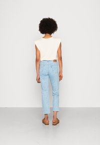 Vit ärmlös topp, blå randiga högmidjade jeans och bruna plattformssandaler. Jeansarna har ett texturerat mönster och en bakficka.