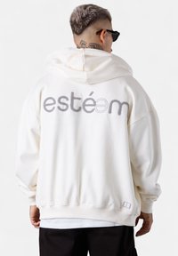 Haut à capuche surdimensionné blanc avec "estém" brodé en gris au dos, doté d'une capuche à cordon de serrage et de poignets et ourlet côtelés.