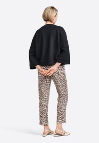 Czarny krótki sweatshirt z szerokimi rękawami w poł�ączeniu z beżowymi spodniami w panterkę. Modelka stoi z rękami skrzyżowanymi za plecami.