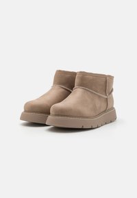 Botines de ante en tono tostado con punta redondeada, costuras decorativas y suela de goma con ranuras horizontales para mayor tracción.
