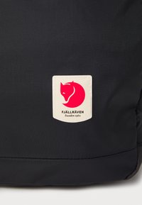 Czarny plecak z tkaniny z wyraźną białą i czerwoną naszywką logo Fjällräven z motywem lisa. Gładka tekstura, trwałe detale szwów.