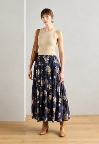 Beige ermeløs topp kombinert med et langt, marineblått blomstermønster skjørt med lagdelt design. Brune ankelstøvler fullfører antrekket.