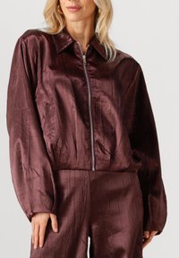 Bordeaux satin bomberjack met een ritssluiting aan de voorkant, een opgevouwen kraag en gestructureerde strepen. Heeft lange mouwen en een elastische zoom.