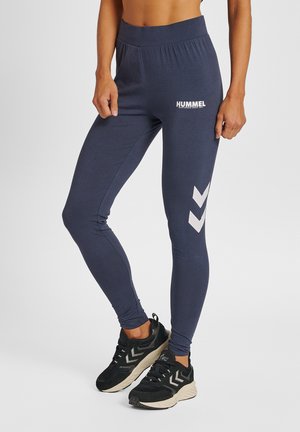 Navy leggings van rekbaar materiaal zijn voorzien van een hoge tailleband, een wit logo en witte chevronpatronen op de kuiten. Inclusief een paar zwarte sneakers.