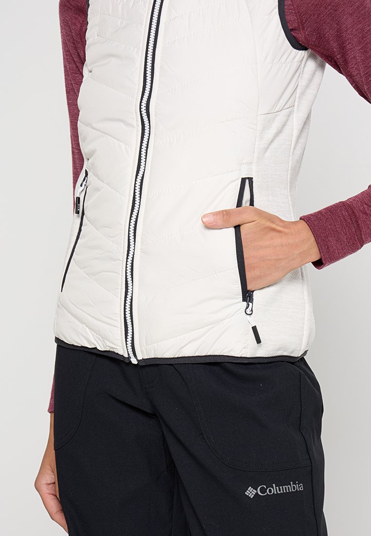 Gilet imbottito leggero senza maniche di colore panna con motivo trapuntato, zip nera e due tasche laterali. Indossato sopra una maglietta a maniche lunghe color bordeaux.