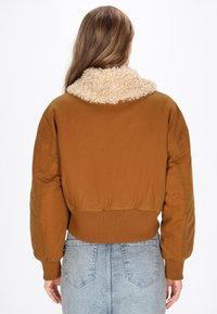 Giubbotto bomber marrone con un colletto beige peloso, orlo e polsini a costine. Materiale liscio e opaco con una vestibilità rilassata e spalle scese.