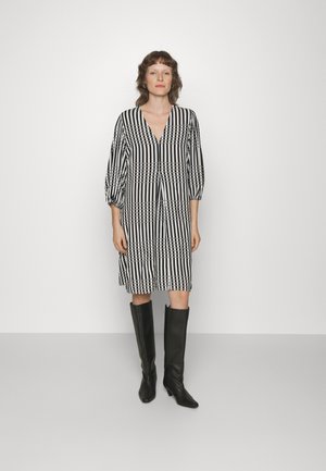 Svart og hvit stripete kjole med V-hals, klokkeærmer og knelangen cut. Båret med høye svarte støvler. Glatt stoffstruktur.