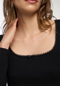 Czarna bluzka z dekoltem w serek, ozdobionym falbaną i małą kokardką. Długie rękawy z teksturowanej tkaniny.