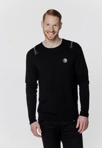 Czarny, długi rękaw koszulka z zamkami na ramionach i okrągłym logo na klatce piersiowej. Gładka tekstura, dopasowany krój i okrągły dekolt.