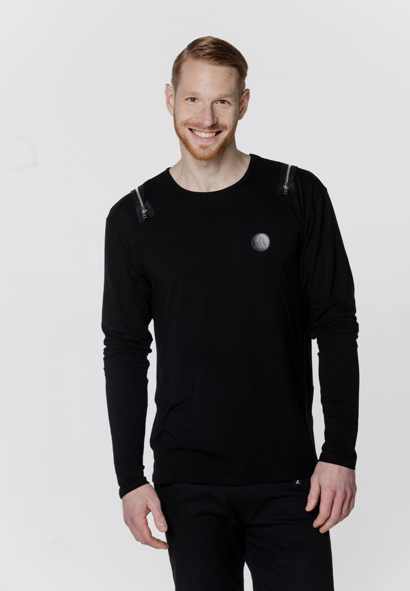 Czarny, długi rękaw koszulka z zamkami na ramionach i okrągłym logo na klatce piersiowej. Gładka tekstura, dopasowany krój i okrągły dekolt.