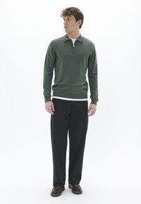 Zeleni pleten žepni pulover z oblikovanim ovratnikom, nosi se čez belo srajco, v kombinaciji s črnimi hlačami in temnimi čevlji.