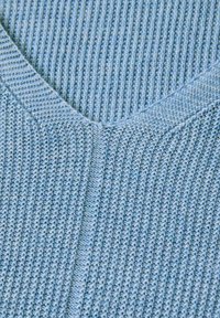 Hellblau gestrickter Pullover mit V-Ausschnitt, strukturiertem Rippmuster und aus weichem, atmungsaktiven Material mit subtilen Farbvariationen.