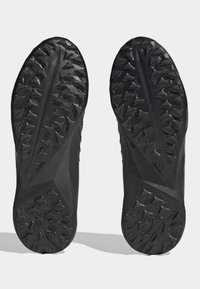 Svart skosula med en texturerad yta med triangulära nitar för grepp, en slät mittsektion och en subtil detaljerad logotyp.