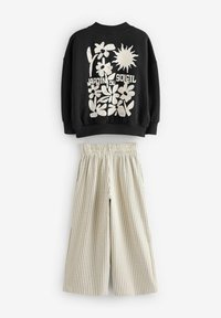 Sweatshirt noir avec un graphique floral et un soleil blanc, présentant un col côtelé. Pantalon large crème avec des rayures verticales et une taille élastique.