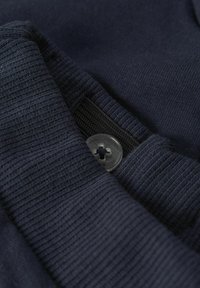 Tissu bleu marine avec une texture côtelée et une surface lisse. Comprend un bouton en plastique et une étiquette en tissu noir.