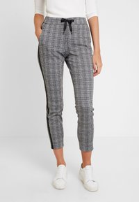 Czarno-białe spodni w kratę z elastyczną talią, sznurkiem do wiązania i czarnymi paskami po bokach. Posiadają dwie kieszenie boczne oraz zwężany krój.