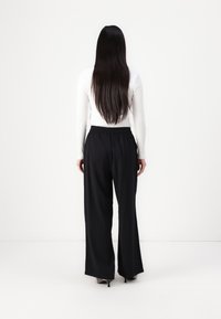 Black wide-leg trousers with an elastic waistband, paired with a fitted white long-sleeve top, viewed from the back. Smooth texture.
