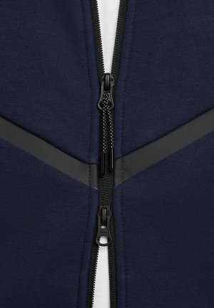 Felpa blu navy con zip, dotata di cerniere e dettagli neri, caratterizzata da una texture in tessuto morbido e da un sottogrilaggio bianco a contrasto.