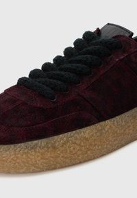 Sneakers en daim bordeaux avec lacets noirs, semelle en caoutchouc texturée et détails cousus sur le dessus pour une touche de design supplémentaire.