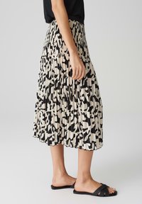 Gonna midi plissettata in crema con un audace motivo astratto nero. Vita elastica, tessuto leggero e una silhouette fluida per il massimo comfort.