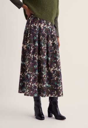 Woman wearing a floral patterned midi skirt with gathered waist, black heeled boots, and a green sweater over a long-sleeve gray shirt.
