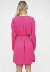 Vaaleanpunainen pitkähihaiminen mekko, jossa on rento istuvuus, joustava vyötärönauha ja sileä kangaspinta. Mekko ulottuu polven yläpuolelle ja siinä on pyöreä pääntie.