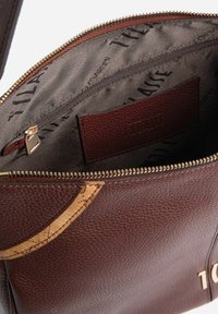 Borsa di pelle marrone con apertura con zip, caratterizzata da una finitura testurizzata. L'interno presenta una fodera in tessuto liscia e una piccola tasca con zip.