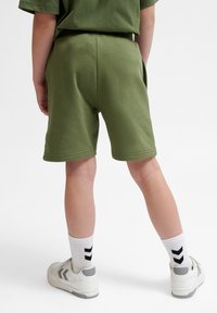 Gröna bomullsshorts med en avslappnad passform, med sidofickor och en mjuk yta. Matcher med vita sneakers och svartsrandiga strumpor.