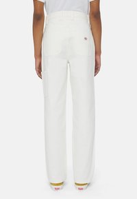 Vita vida-byxor gjorda av kraftigt material, med bakfickor och en sidoficka för verktyg. Synlig sömnad och design med bälteshål.