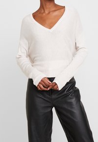 Ljusbeige v-ringad tröja med ribbad textur och långärmar, ihop med svarta läderbyxor, som visar en avslappnad passform.