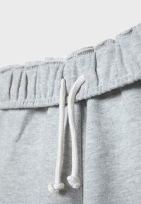 Gros plan de la taille d’un pantalon de survêtement gris clair avec élastique et cordons blancs pendants.