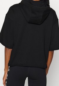 Svart oversized hoodie med mjuk textur, korta ärmar och framficka. Inkluderar en dragsko för huvan och sidofyggs.