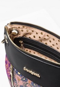 Black handbag with purple and floral fabric panels, gold zipper, and beige interior lining with gold polka dots.