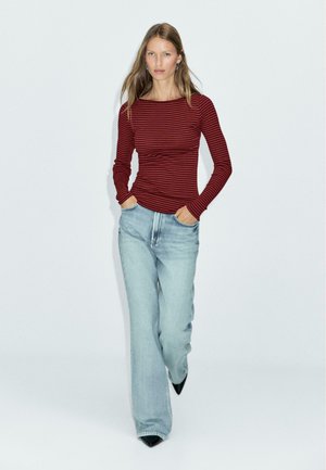Red and black striped long-sleeve top paired with light blue straight-leg jeans. The model wears black pointed-toe heels.