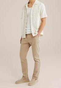 Short-sleeve cream shirt with floral design, paired with light beige pants and beige slip-on shoes. Smooth fabric with relaxed fit.