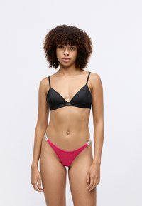 Bralette noir en triangle avec bretelles ajustables et détail de logo ; associé à un string rose avec une taille contrastante. Texture de tissu lisse.