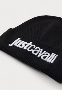 Črna rebrasta kapa z belim vezenim logotipom "justcavalli". Mehka tekstura, prilegajoča zasnova in zavit rob.