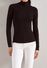 Zwarte lange mouwen turtleneck van zachte gebreide stof, aansluitend ontwerp en een soepele textuur. Gecombineerd met witte slim-fit broek.