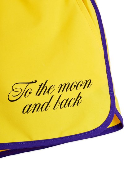 Tissu jaune avec bordure violette affichant un texte en cursive noire « Jusqu'à la lune et retour » imprimé dans le coin inférieur.