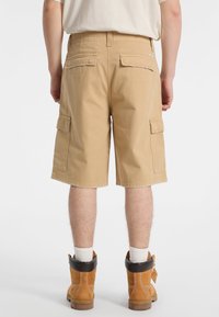 Shorts cargo beiges avec deux poches latérales et deux poches arrière, en coton, avec une coupe droite et un ourlet effiloché.