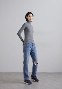 Grå turtleneck-genser kombinert med slitte lyseblå jeans. Modellen har på seg navy joggesko. En enkel bakgrunn fremhever antrekket.