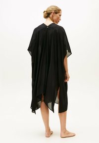 Kaftano nero fluente con silhouette ampia, realizzato in tessuto leggero. Presenta uno scollo rotondo, maniche corte e spacchi laterali alti.