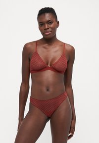 Rotes Netz-Lingerie-Set bestehend aus einem Bralette und einem passenden Tanga, beide mit einem Herzmuster und zarten Besatzdetails.