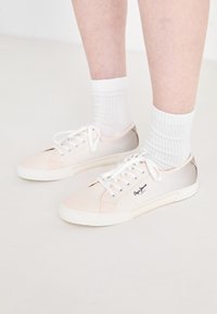 Sneakers in tela chiara con lacci bianchi, caratterizzati da dettagli rosa e beige, suola in gomma bianca e logo sul lato.