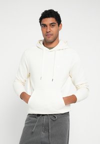Biała bluza z kapturem z przednią kieszenią, troczkami i małym detalem logo. Miękki materiał i dopasowane rękawy dla casualowego wyglądu.