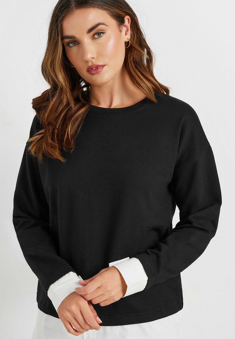 Musta huppari pitkilla hihoilla, pyöreällä kauluksella ja valkoisilla hihansuilla. Pehmeä kangas, jossa on rento leikkaus, ja siinä on minimaalinen muotoilu ilman kuoseja.