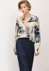 Multi-colored, long-sleeve shirt with an abstract print, button-down collar, and soft fabric. Paired with dark, loose-fitting trousers.