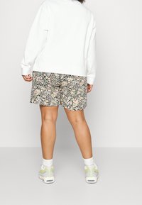 Sweat-shirt blanc et short noir à motifs floraux. Le mannequin porte des chaussettes blanches et des baskets légères avec des accents jaunes et bleus.