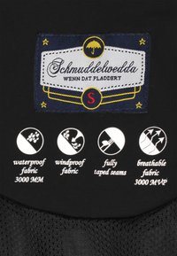 Fekete ruhacímke „Schmuddelwedda” felirattal és esernyő grafikával, amely vízálló, szélálló és légáteresztő anyagot jelöl.